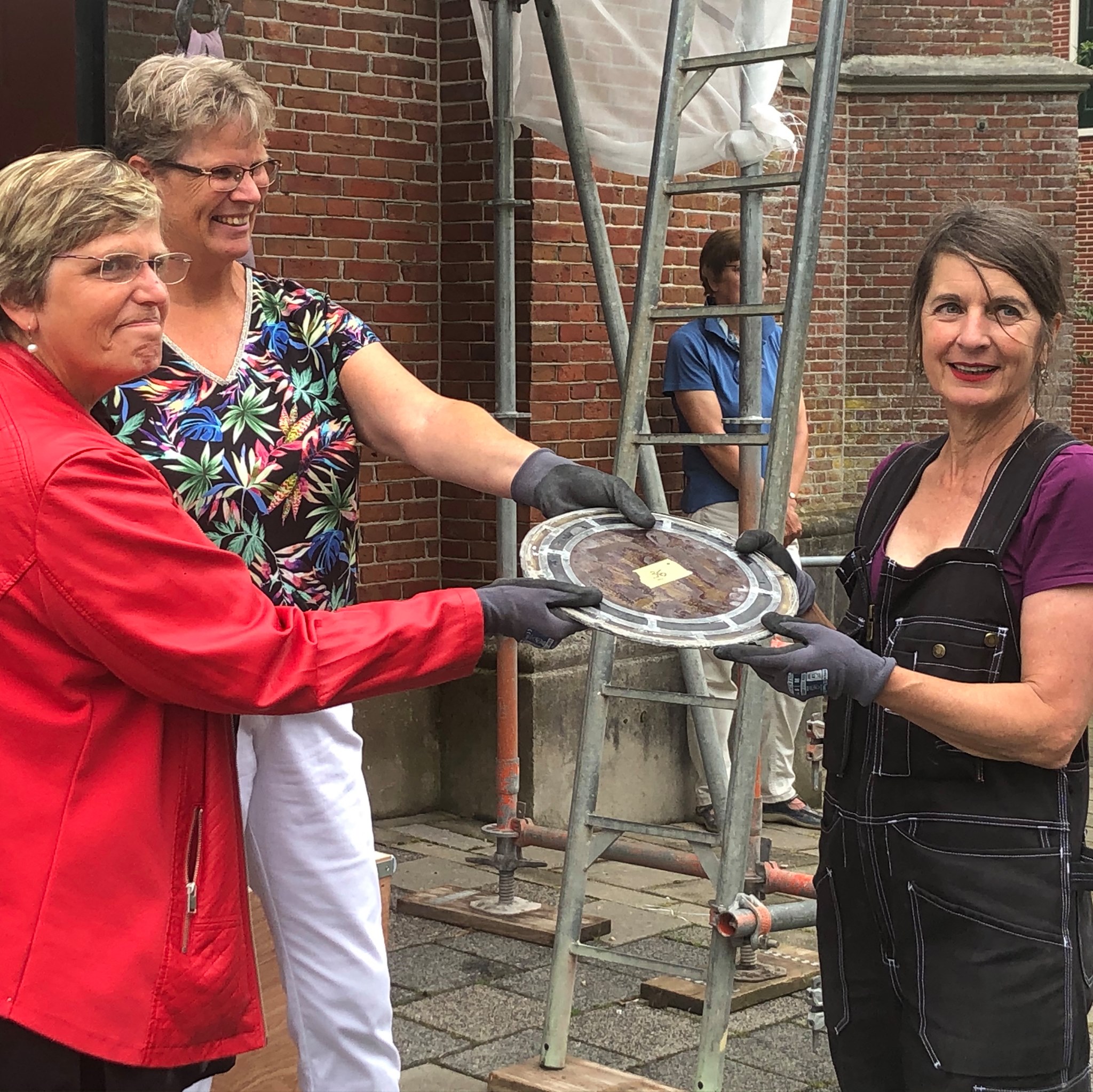 Pastor Nellie Hamersma - Sluis (links) overhandigt het eerste glas in lood raam aan de restauratrice.