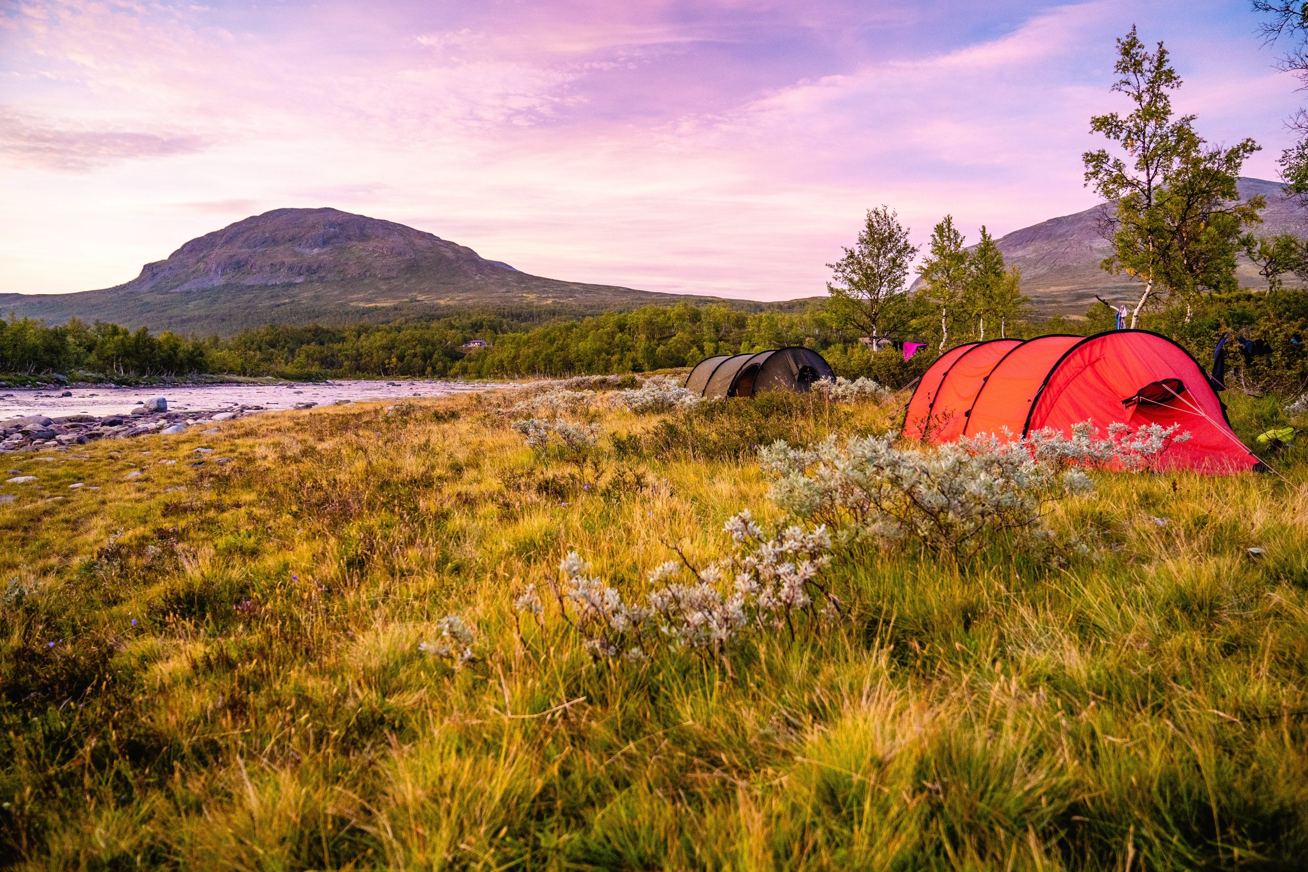 A field with tents surrounded by hills covered in greenery under a cloudy sky during the sunset